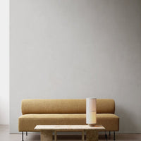 Tan textured sofa with minimalist design, paired with a sleek white lamp on a light marble table against a neutral wall.