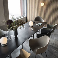 Modern dining setup featuring pastel chairs, sleek black table, and wooden paneled wall accents. Elegant and minimalist design.