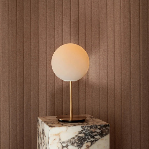 Minimalist round lamp with soft amber shade on textured brown wall with vertical stripes and marble base.