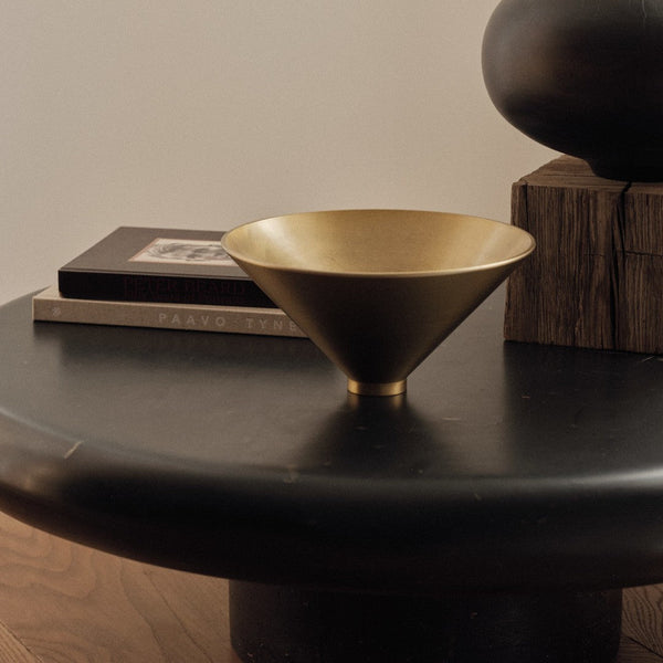 "Modern gold cone bowl on a sleek black table; elegant metallic finish enhances contemporary decor."