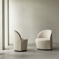 Beige upholstered chairs with smooth curves and a sleek black base, set against a minimalist backdrop.