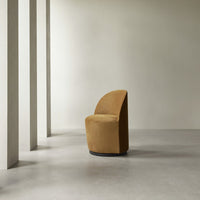 Curved mustard yellow chair on a smooth gray floor, featuring a minimalist design against a neutral backdrop.