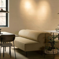 Beige curved sofa paired with dark wood dining chairs, set against a neutral wall and subtle greenery.