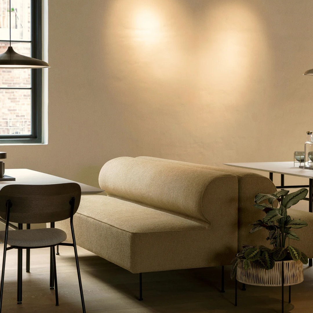 Beige curved sofa with a smooth texture, surrounded by dark wood and greenery, enhancing a cozy, modern aesthetic.
