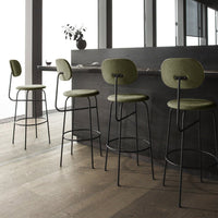 Green upholstered bar stools with black metal frames, set against a minimalistic wooden floor backdrop.
