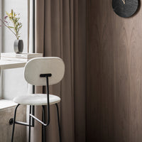 Stylish white bar stool with black metal legs against warm, neutral-toned wooden wall and soft brown curtains.