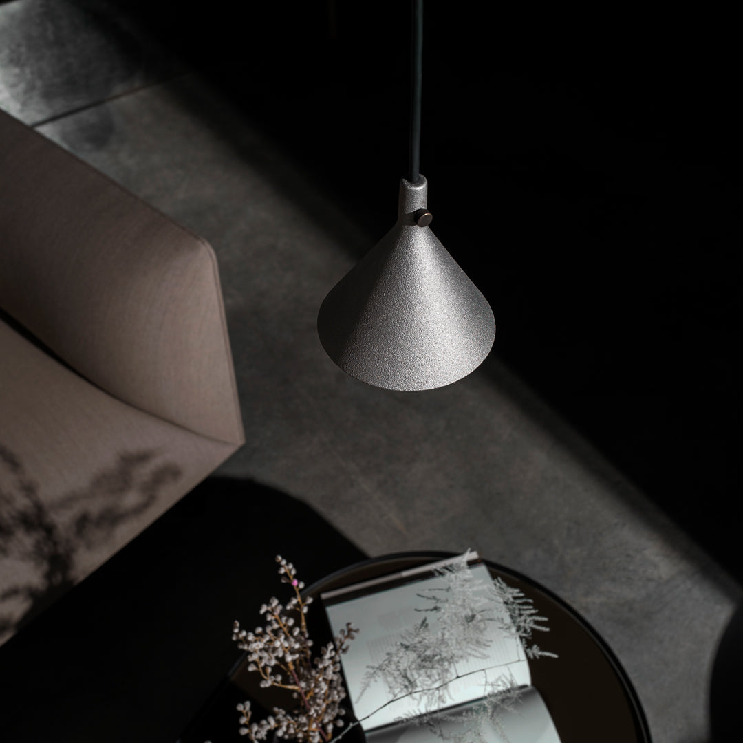 "Modern silver pendant lamp with a sleek conical design, illuminating a cozy, dark-toned living space."