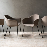 Beige upholstered chairs with curved backs and black metal legs against a textured gray wall. Soft neutral tones.