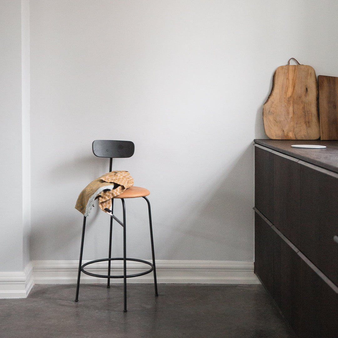 Black metal stool with a tan cushion, set against a neutral-colored wall and dark wood cabinetry.