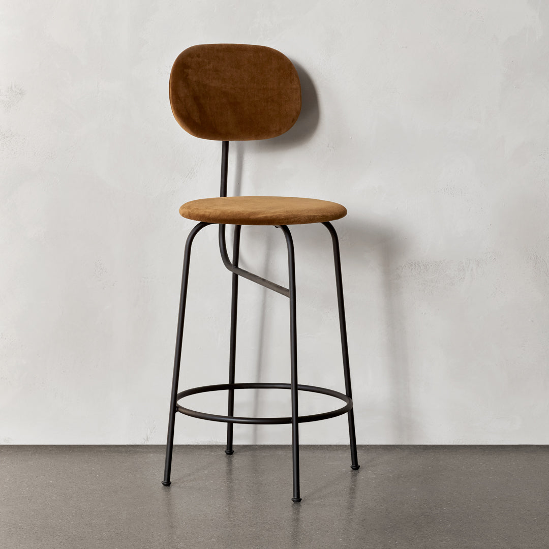 Brown upholstered stool with a rounded back and sleek black metal legs against a light gray background.