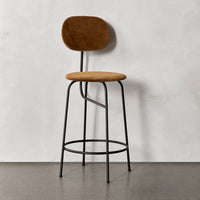 Brown upholstered stool with a rounded back and sleek black metal legs against a light gray background.