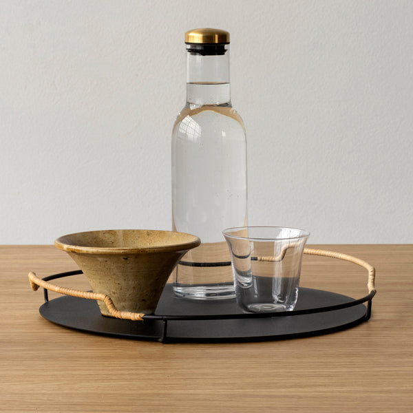 "Matte black tray with natural bamboo accents, featuring a textured ceramic bowl and clear glass cup."