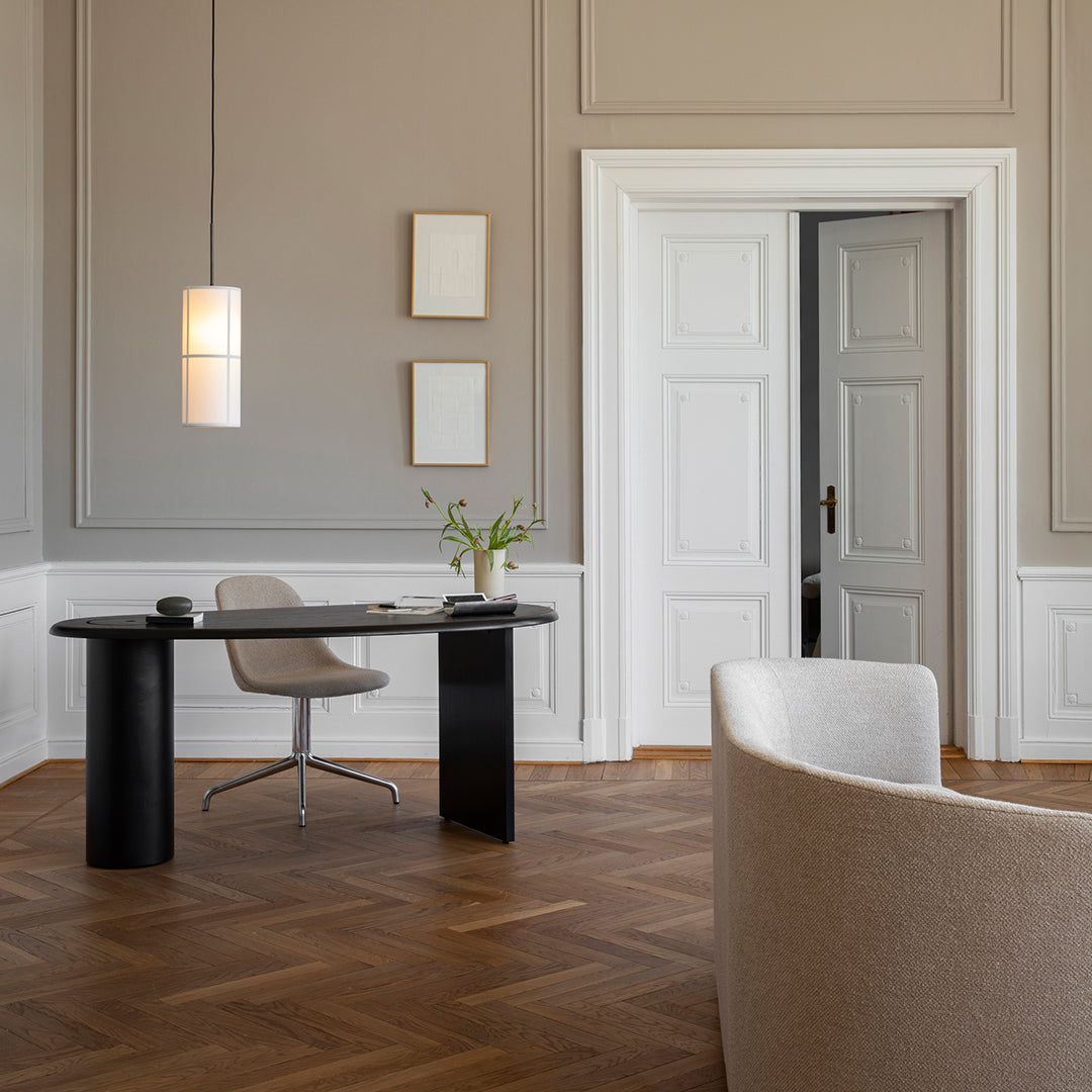 Modern workspace featuring a soft beige chair, black oval desk, and natural wood herringbone flooring against gray walls.