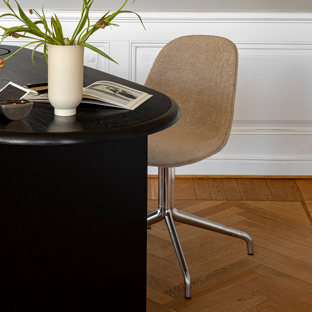 Beige upholstered chair with a smooth texture, set against a sleek black table and warm wooden floor.