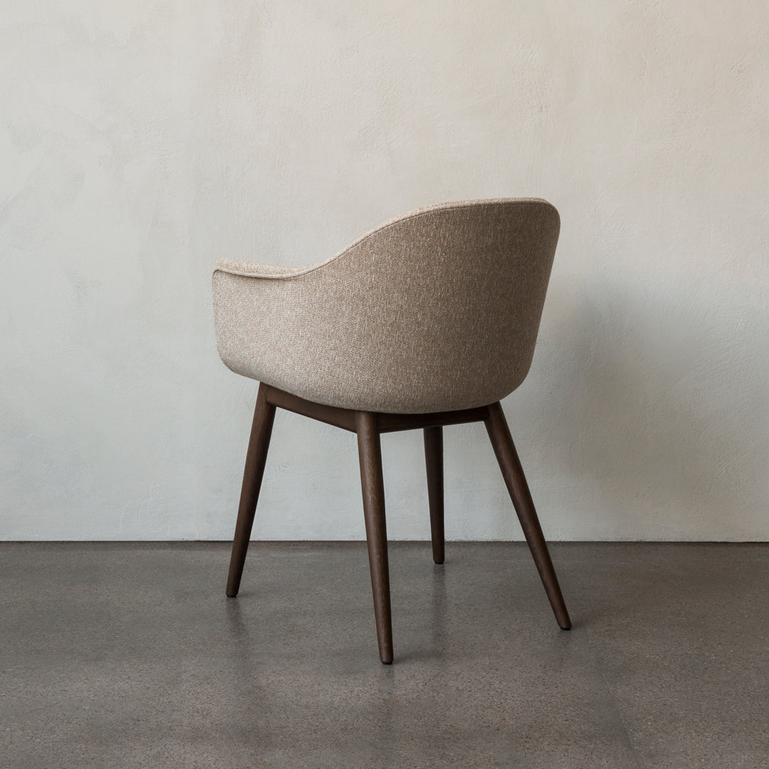 Beige upholstered chair with a subtle pattern and dark wooden legs against a neutral wall.