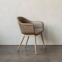 Modern brown leather armchair with natural wood legs against a light textured wall. A stylish addition to any space.