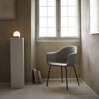 Gray upholstered chair with sleek black legs, set against a soft beige wall and warm wooden floor. Modern minimalist design.