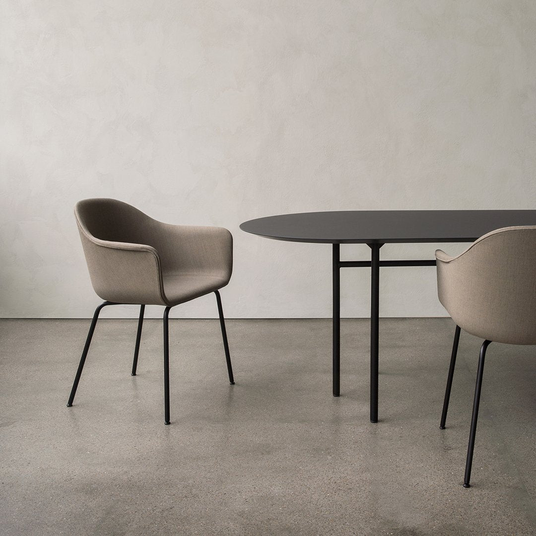 Beige upholstered chairs with sleek black metal legs beside a modern, oval black table on a gray concrete floor.