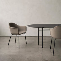 Beige upholstered chairs with sleek black metal legs beside a modern, oval black table on a gray concrete floor.