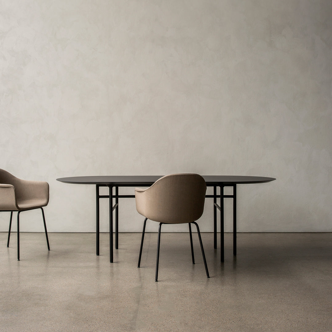 Elegant black oval dining table with beige upholstered chairs on a light textured background. Modern minimalist design.