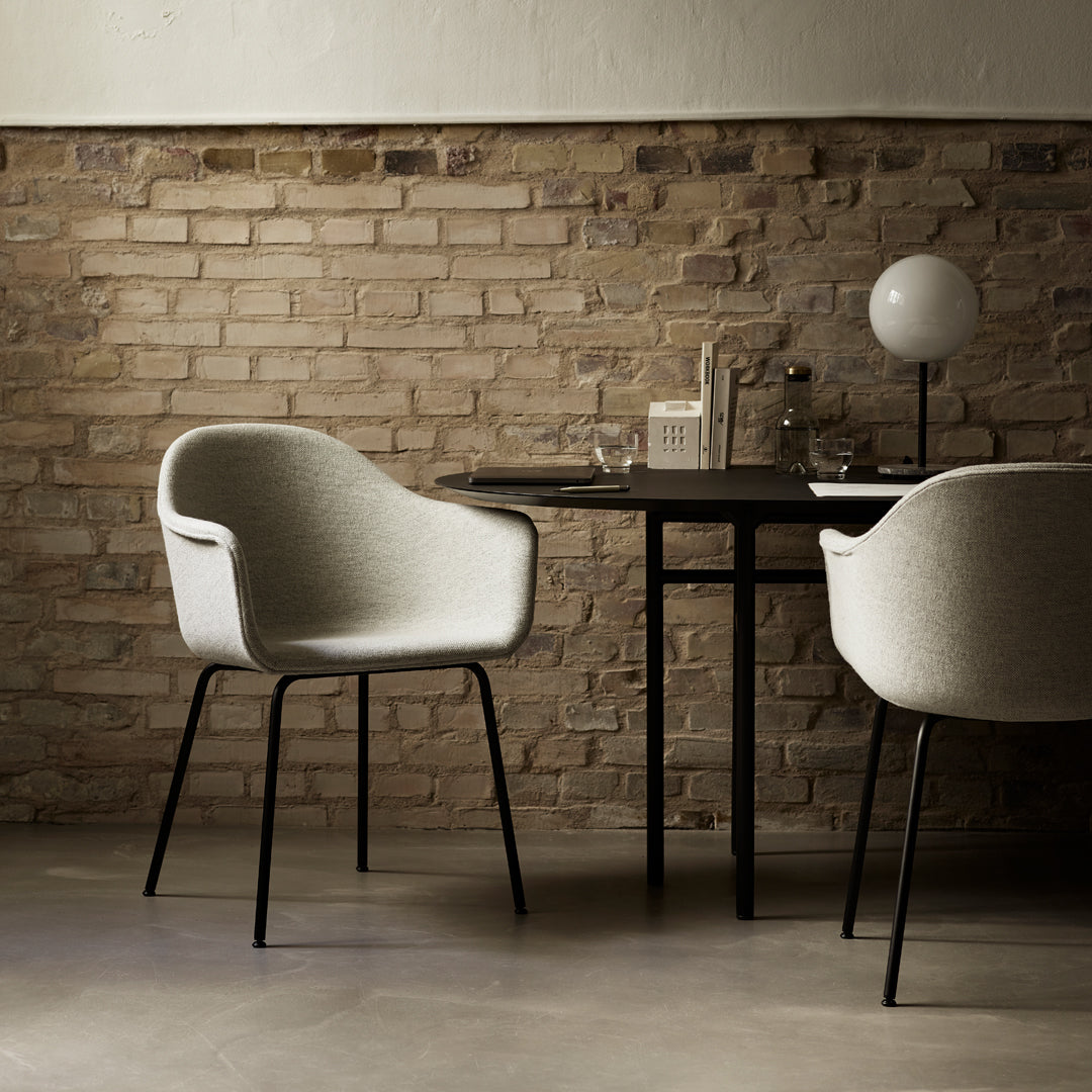 Gray upholstered chair with black metal legs, set against a rustic brick wall in a minimalist dining space.