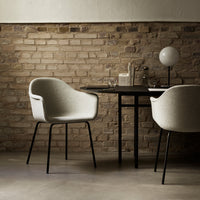 Gray upholstered chair with black metal legs, set against a rustic brick wall in a minimalist dining space.
