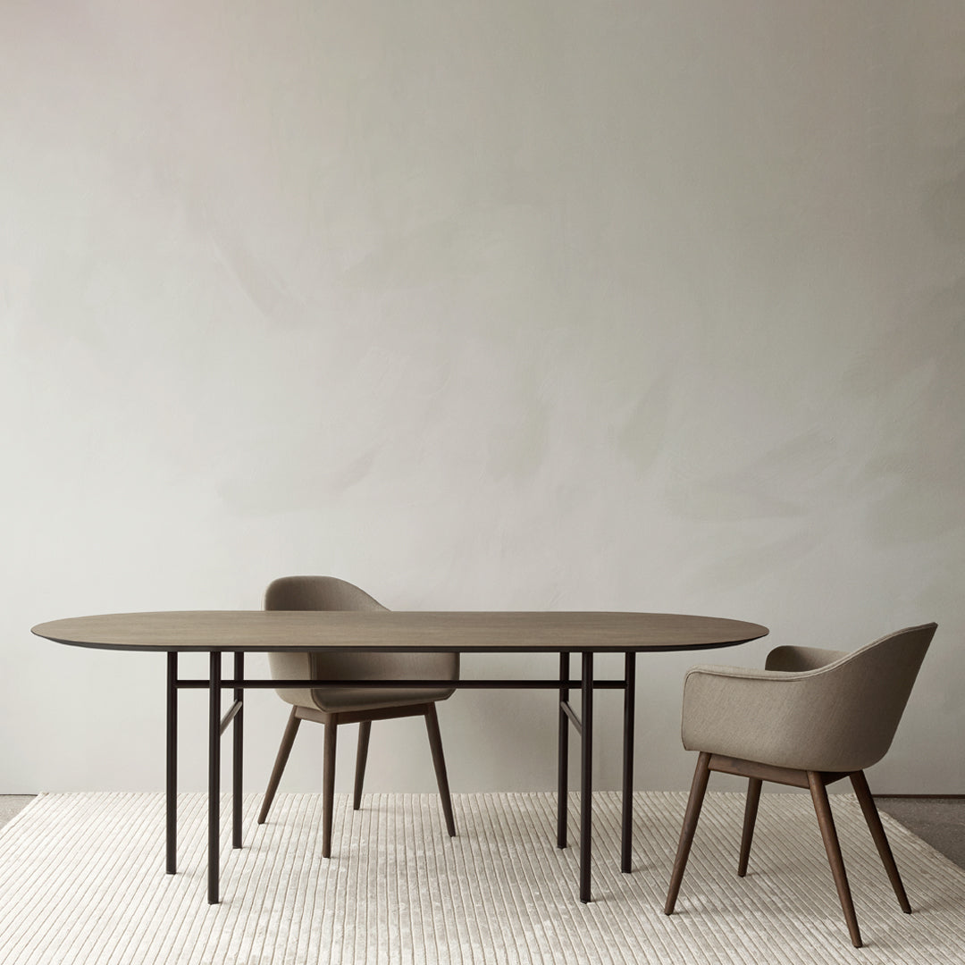 Modern oval table in earthy brown with soft beige upholstered chairs on a textured light rug against a neutral wall.