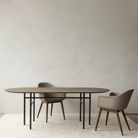 Modern oval table in earthy brown with soft beige upholstered chairs on a textured light rug against a neutral wall.