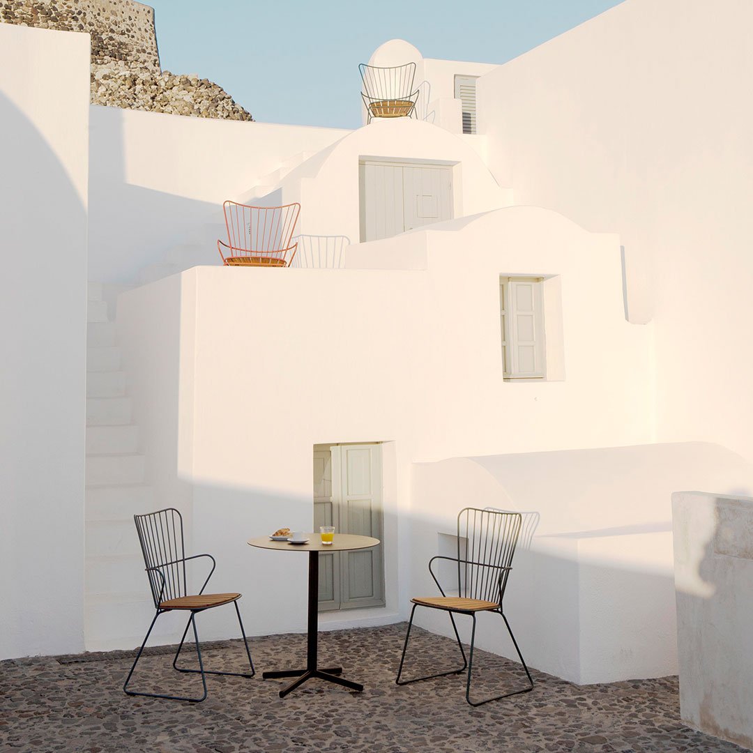 Modern patio set featuring black metal chairs with wooden accents and a round yellow table against a whitewashed backdrop.
