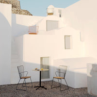 Modern patio set featuring black metal chairs with wooden accents and a round yellow table against a whitewashed backdrop.