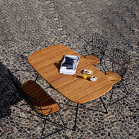 Brown striped wood table with black metal chairs set against a textured stone surface. Stylish outdoor dining.
