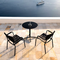 Black striped chairs and a round black table atop a light-toned tiled patio overlooking the water.