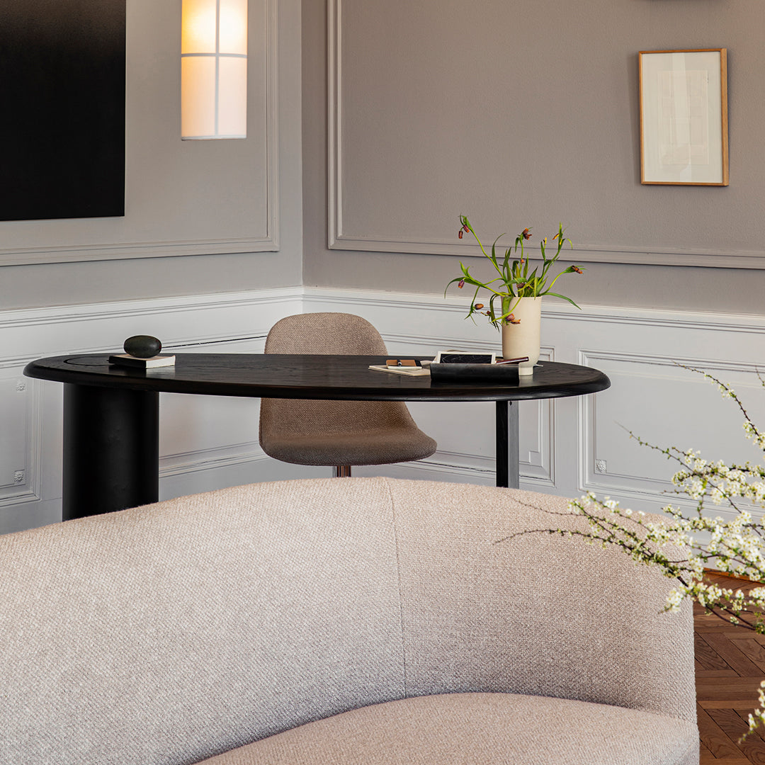 Modern black round desk against a soft gray wall, accented by a light beige chair and textured neutral sofa.