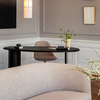 Modern black round desk against a soft gray wall, accented by a light beige chair and textured neutral sofa.