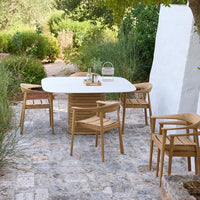 Light wood dining set with a white tabletop, surrounded by lush greenery and stone patio for a serene outdoor vibe.