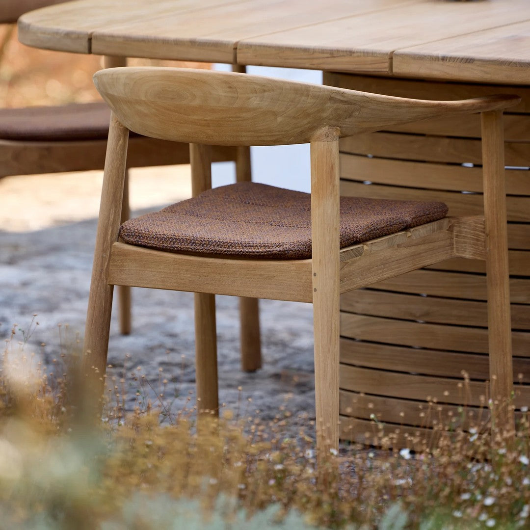 Natural wood chair with a brown upholstered seat, featuring a smooth design and earthy tones in an outdoor setting.