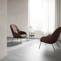 "Plush brown armchairs with sleek black legs, set against a minimalist gray floor and bright, soft curtains."