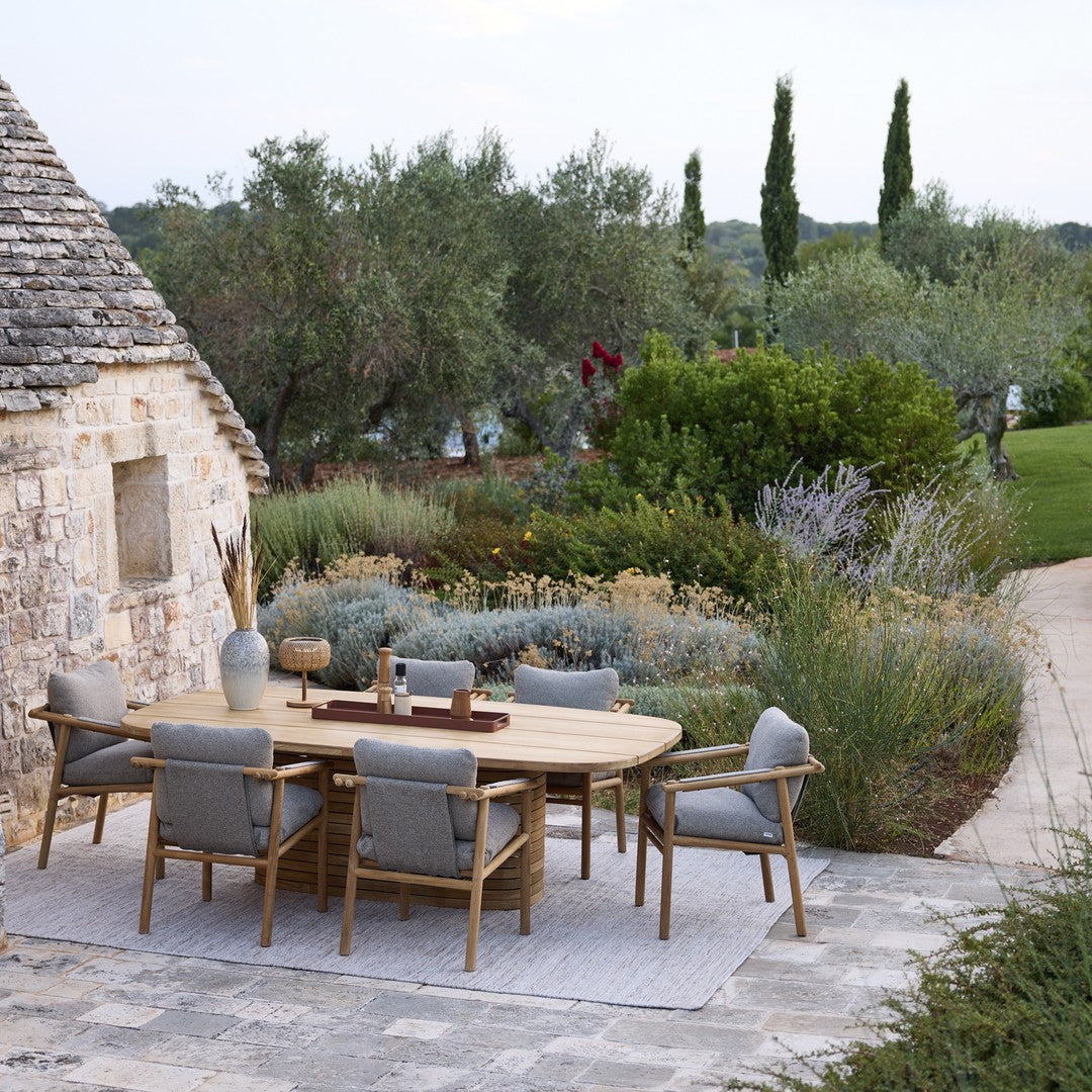 "Outdoor dining set featuring natural wood tones and soft gray cushions against a lush green garden backdrop."