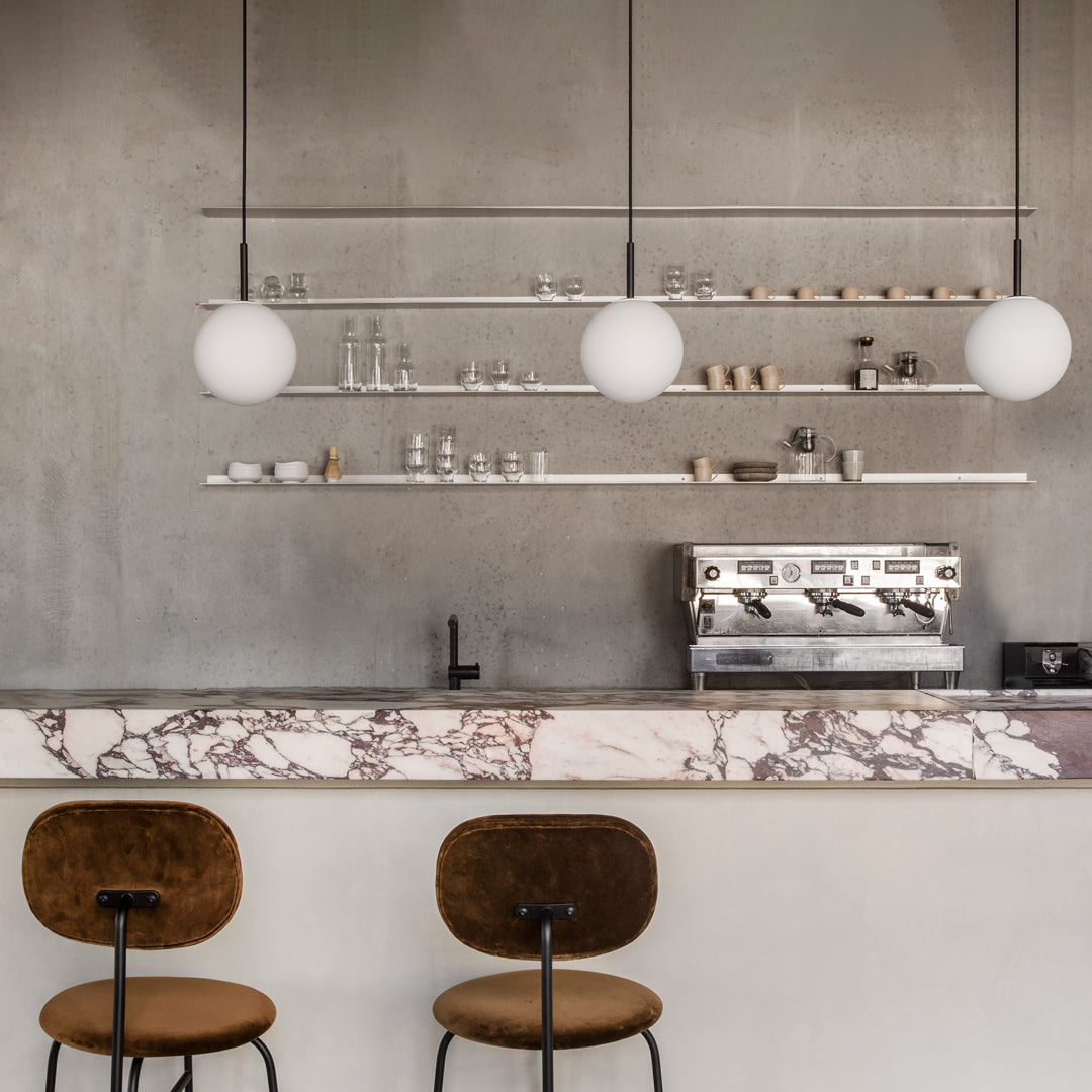Modern coffee bar with a grey concrete backdrop, marble countertop, and minimalist white globe pendant lights.