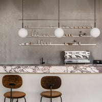 Modern coffee bar with a grey concrete backdrop, marble countertop, and minimalist white globe pendant lights.