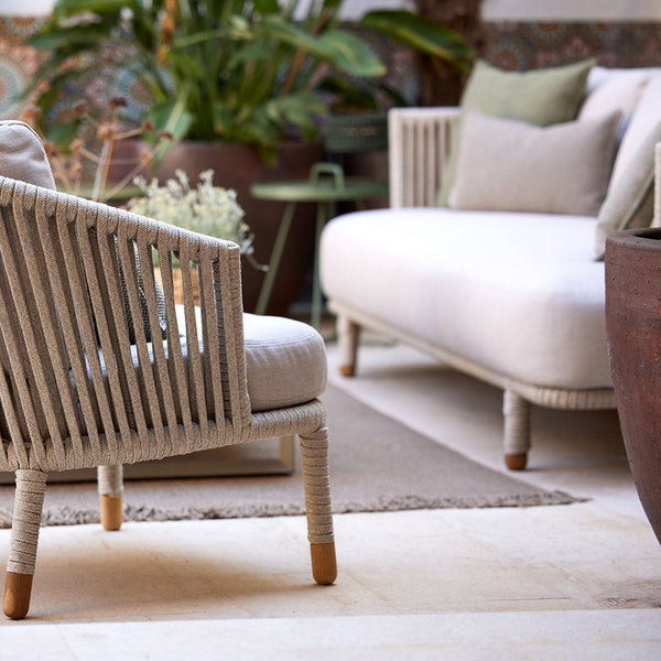 Neutral beige and taupe outdoor furniture with textured patterns, complemented by green cushions and lush greenery.