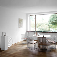 "Modern dining space with white walls, wood flooring, and circular table featuring sleek wire chairs with wooden seats."