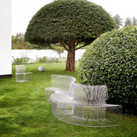 Clear transparent furniture set against a lush green garden, featuring curved lines and modern design.