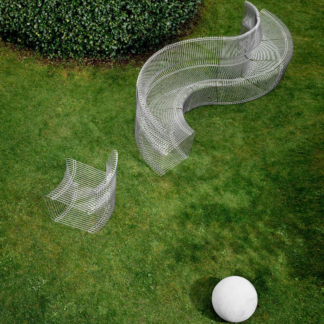 Curved metallic outdoor seating in gray with a whimsical wire mesh pattern on a grassy landscape.