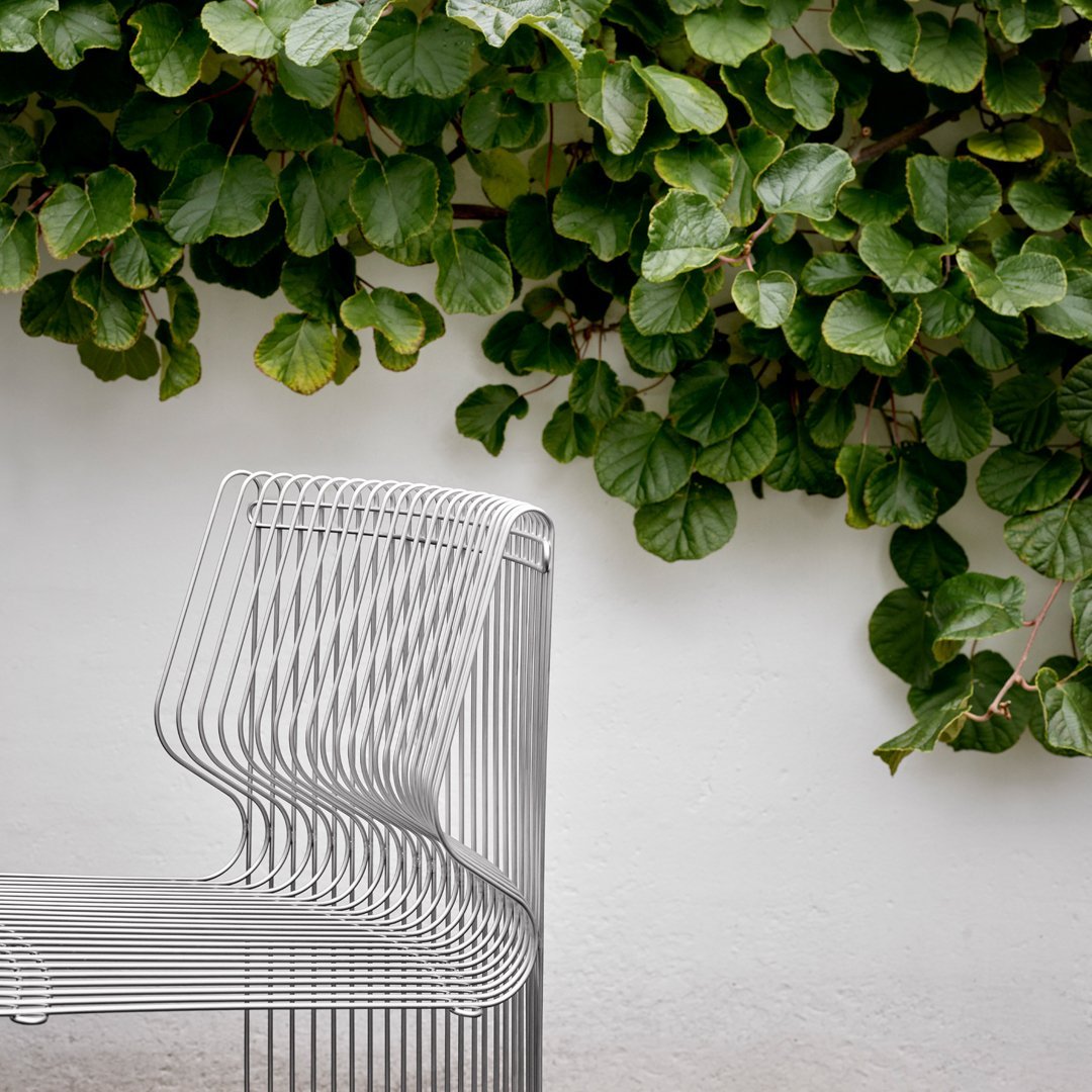 Stylish silver wire chair with a sleek design, contrasted against vibrant green foliage backdrop.