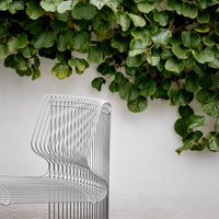 Stylish silver wire chair with a sleek design, contrasted against vibrant green foliage backdrop.