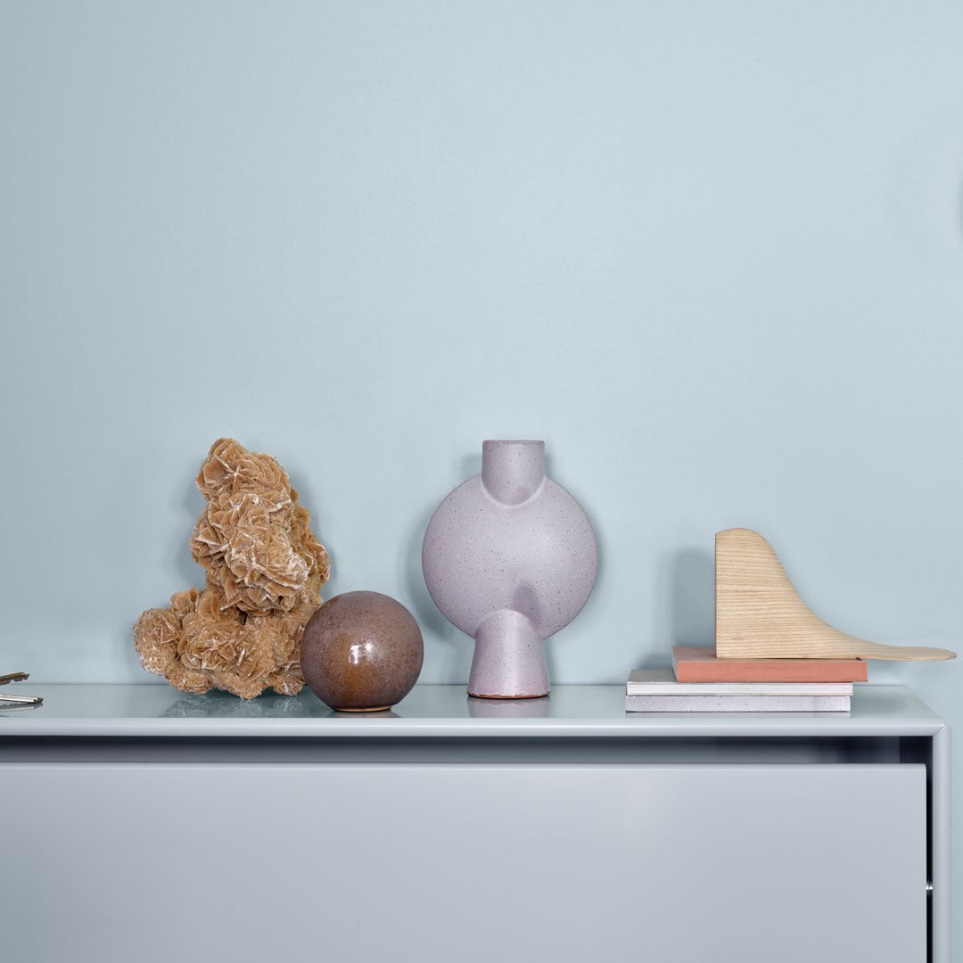 "Decorative vases in soft lavender and brown hues, with a textured natural accent, against a light blue background."