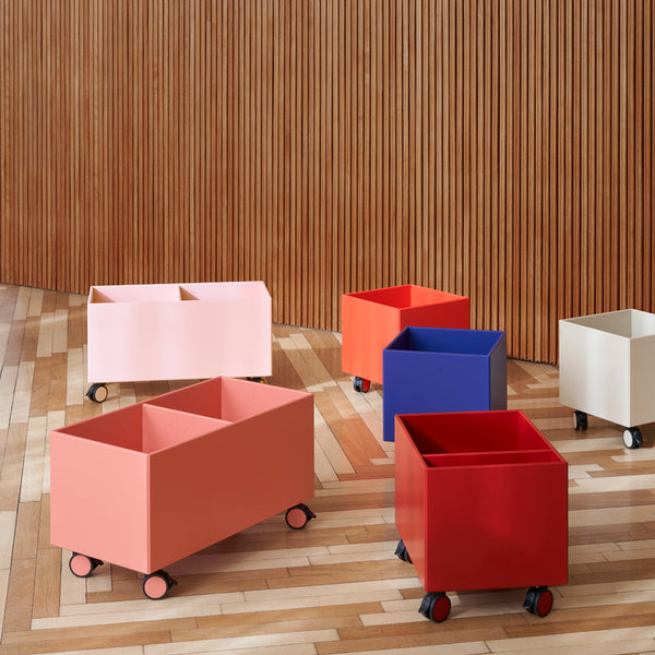 Colorful metal storage bins on wheels in pink, red, blue, and white against a wooden background, showcasing modern design.