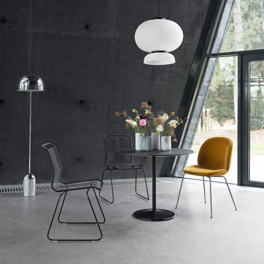 Modern dining room with gray walls, black chairs, a round black table, and a mustard yellow chair, accented by floral arrangements.