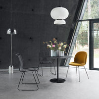 Modern dining room with gray walls, black chairs, a round black table, and a mustard yellow chair, accented by floral arrangements.